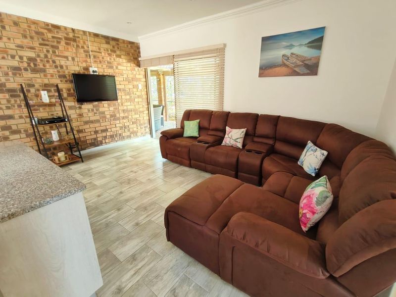 A comfortable living room featuring an exposed brick accent wall, modern tiled flooring, and direct access to an outdoor patio area.