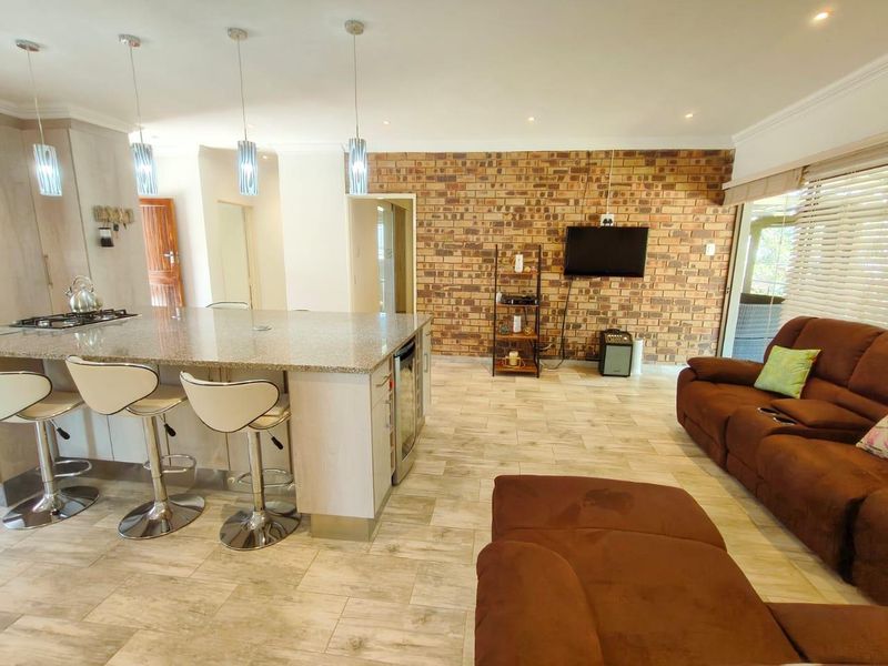 Spacious open-plan living area featuring a modern kitchen with a granite island, gas hob, and a striking exposed brick feature wall.