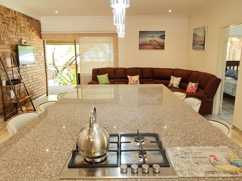 Open plan living area featuring a large granite kitchen island with integrated gas cooktop, exposed brick feature wall, and direct access to the patio.