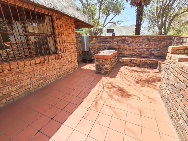 Outdoor patio area featuring a built-in brick braai, tiled flooring, and enclosed by a brick perimeter wall under a thatch roof overhang.