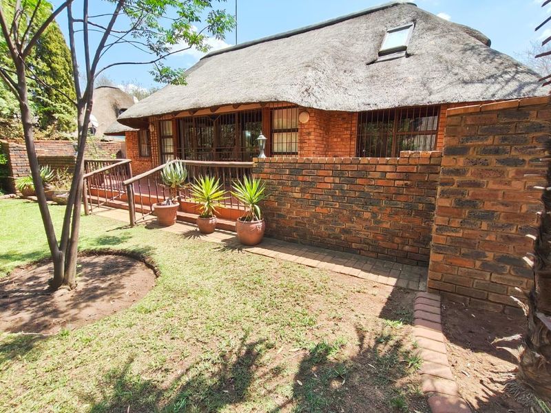 Rear view of a face brick house featuring a traditional thatch roof, raised patio area, and a private garden with brick boundary walls.