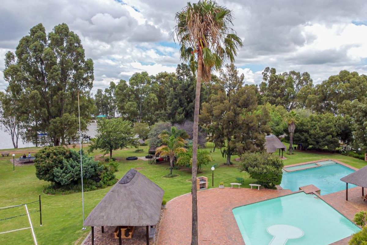 Aerial view of a spacious property featuring a large swimming pool, brick-paved patio, thatched lapa, built-in braai, and expansive landscaped garden grounds.