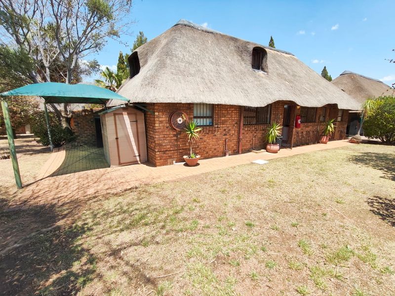 Rear view of a face brick house featuring a traditional thatch roof, security bars on windows, and a paved outdoor area with a shade sail.