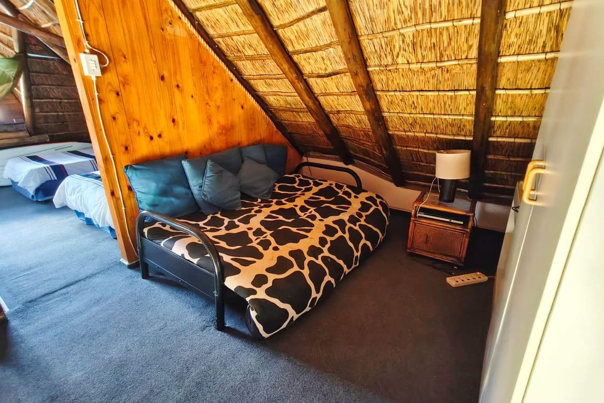 A cozy bedroom featuring a unique thatched roof with exposed timber rafters and warm wood wall paneling, creating a rustic attic-style living space.