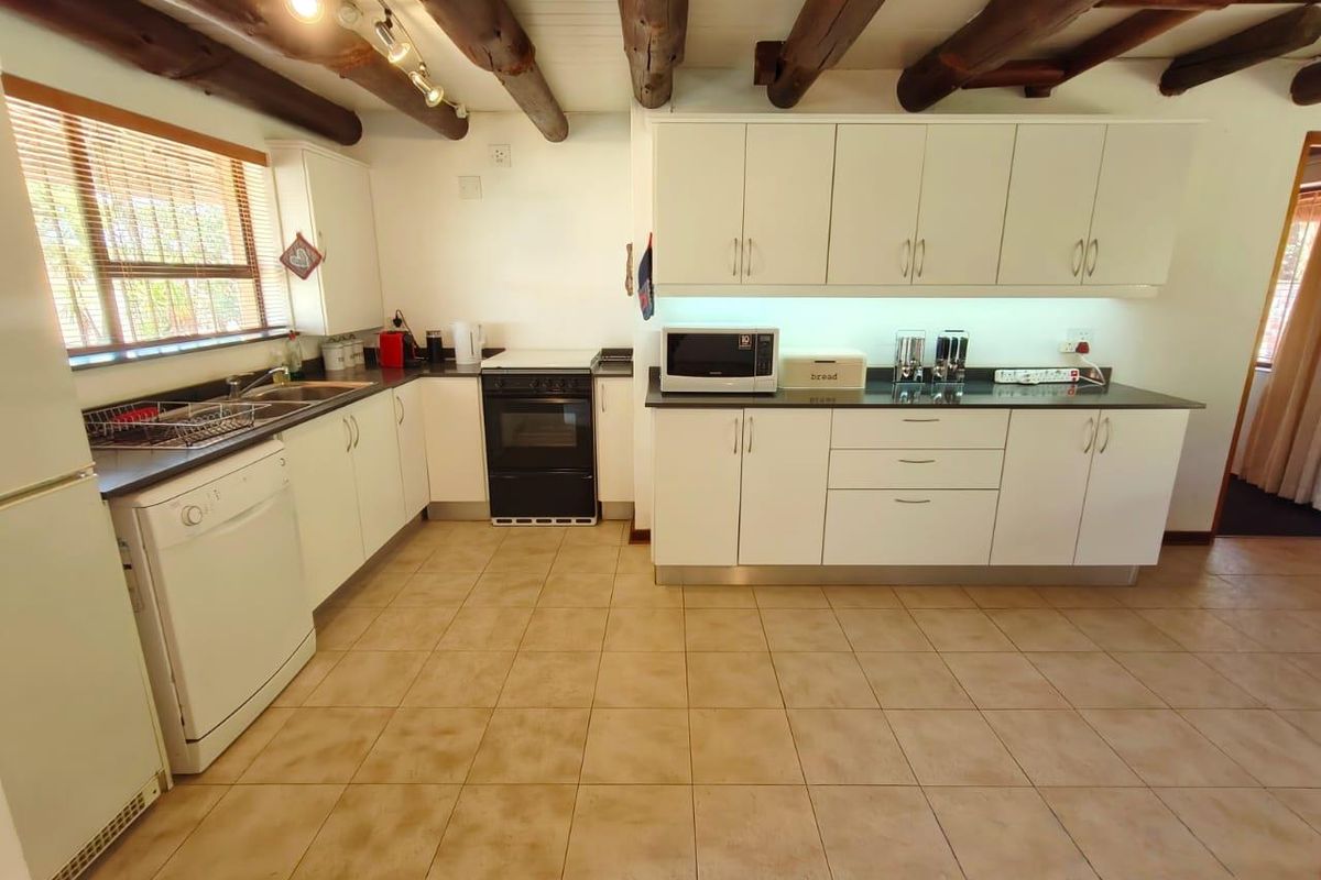 A functional kitchen featuring white cabinetry, dark countertops, and rustic exposed timber ceiling beams, complemented by ceramic floor tiling.