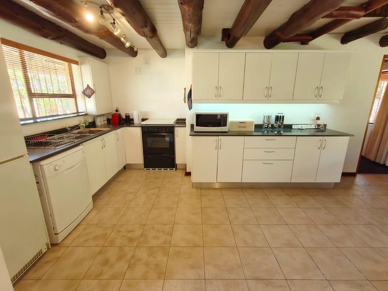 A functional kitchen featuring white cabinetry, dark countertops, and rustic exposed timber ceiling beams, complemented by ceramic floor tiling.