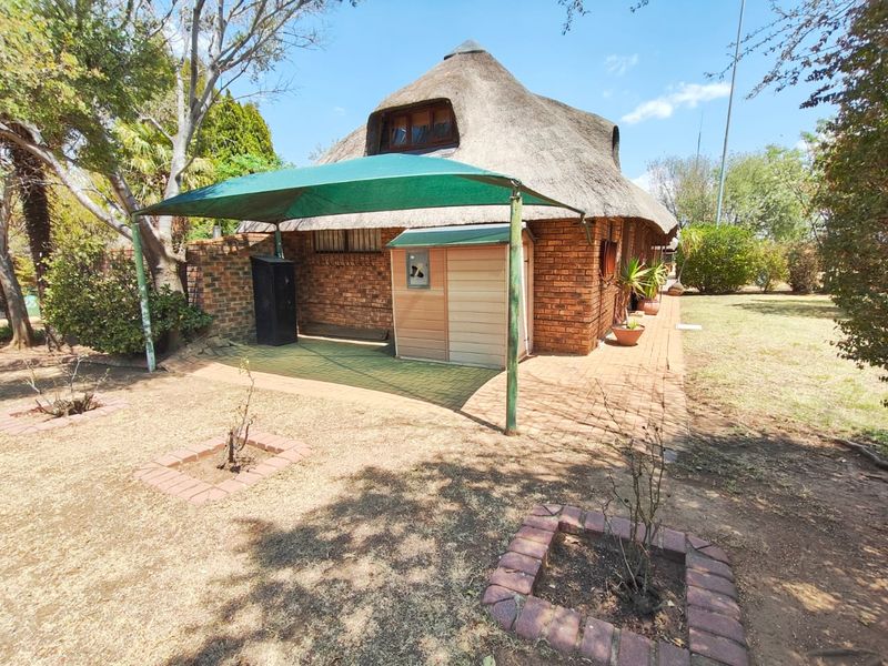 Rear view of a thatched roof house featuring a face brick facade, a paved patio area with a shade sail, and established garden beds.