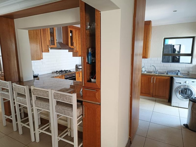 Open plan kitchen featuring wooden cabinetry, granite countertops, subway tile backsplash, and a breakfast bar, with an adjacent scullery area.