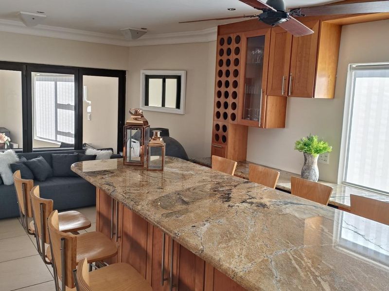 Open plan living and kitchen area featuring a large granite island, wooden cabinetry with integrated wine storage, and access to an outdoor space.