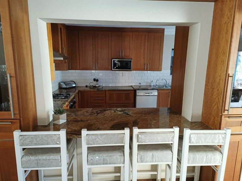 A functional kitchen featuring warm wooden cabinetry, granite countertops, a subway tile backsplash, and a convenient breakfast bar overlooking the space.