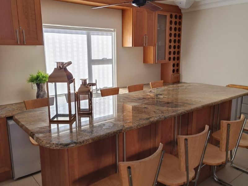 A well-maintained kitchen featuring extensive wooden cabinetry, a large granite-topped breakfast bar, and integrated wine storage.