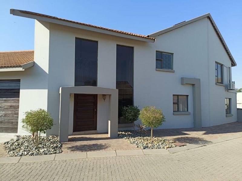A modern double-story residential facade featuring a paved driveway, tiled roof, and a prominent wooden entrance door with tall feature windows.