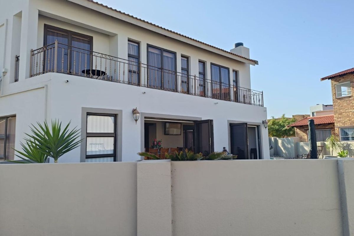 Rear view of a two-story house featuring a spacious upper-level balcony with wrought iron railings and ground-floor access through large sliding glass doors.