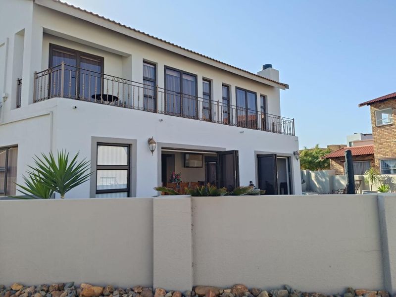 Rear view of a two-story house featuring a spacious upper-level balcony with wrought iron railings and ground-floor access through large sliding glass doors.