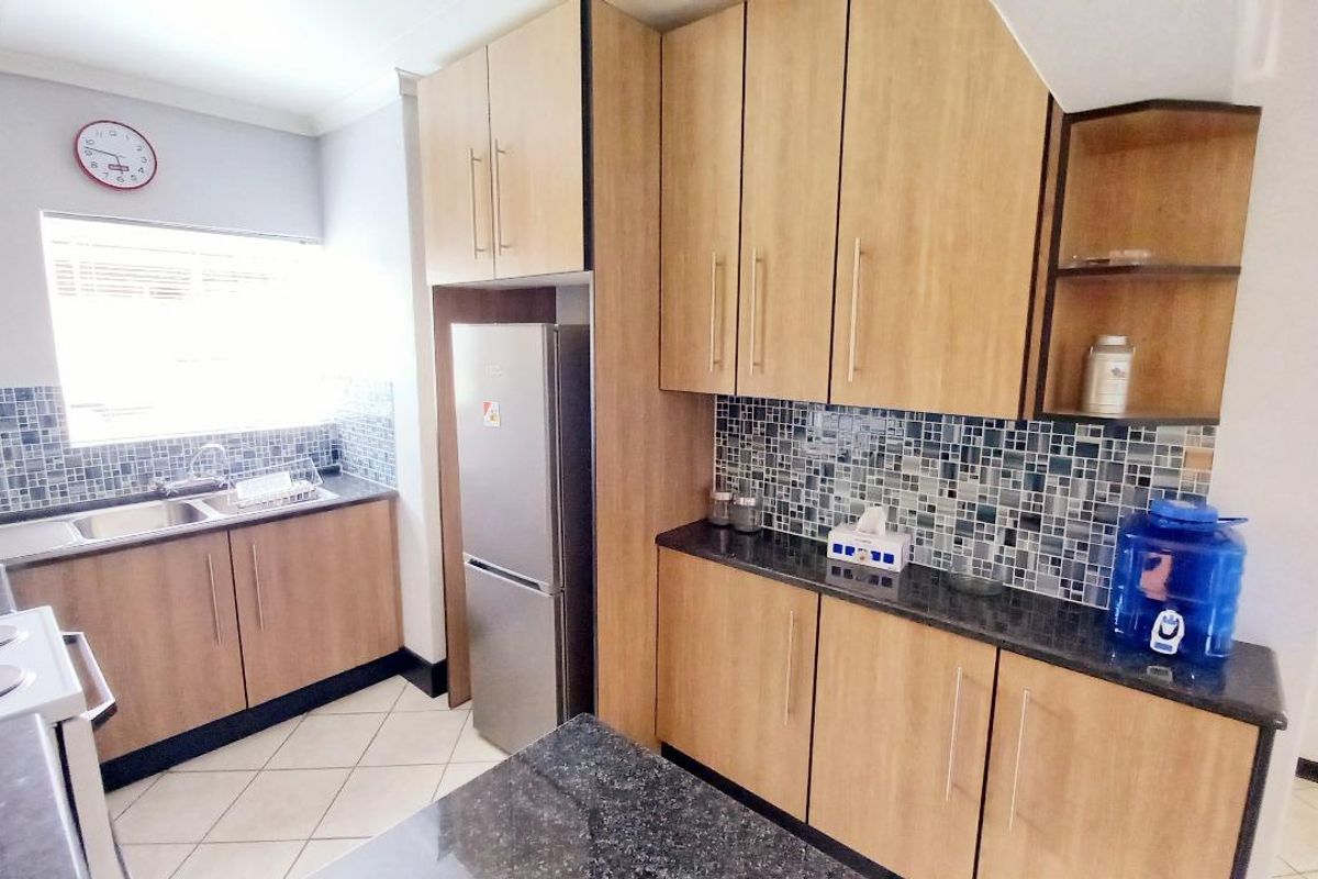 A functional kitchen featuring wood-finish cabinetry, granite countertops, a mosaic tile backsplash, and tiled flooring.