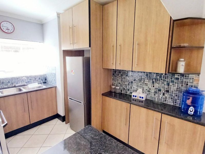 A functional kitchen featuring wood-finish cabinetry, granite countertops, a mosaic tile backsplash, and tiled flooring.