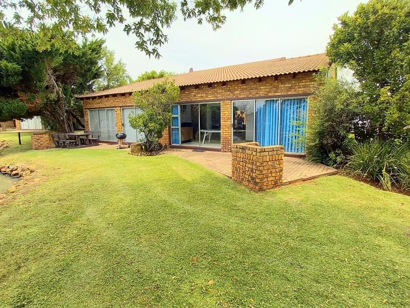 Rear view of a brick house featuring a paved patio area, sliding glass doors, and a well-maintained lawn overlooking a small pond.