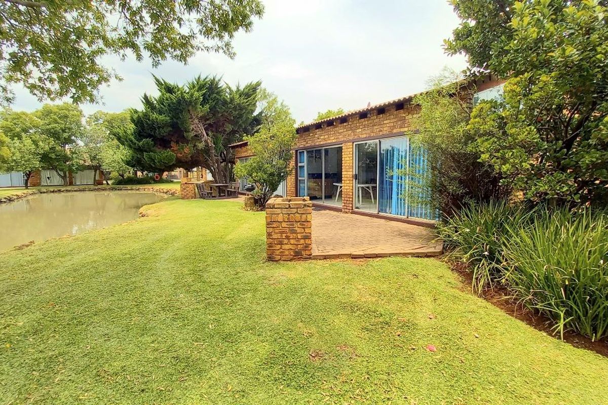 Rear view of a brick house featuring a paved patio area, sliding glass doors, and direct access to a landscaped garden and pond.