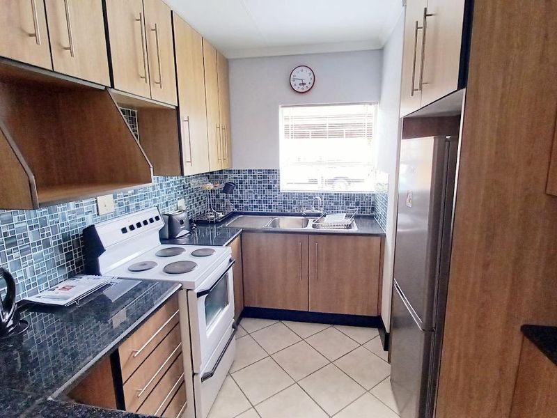 A functional kitchen featuring wood-finish cabinetry, granite countertops, a mosaic tile backsplash, and ceramic floor tiles.