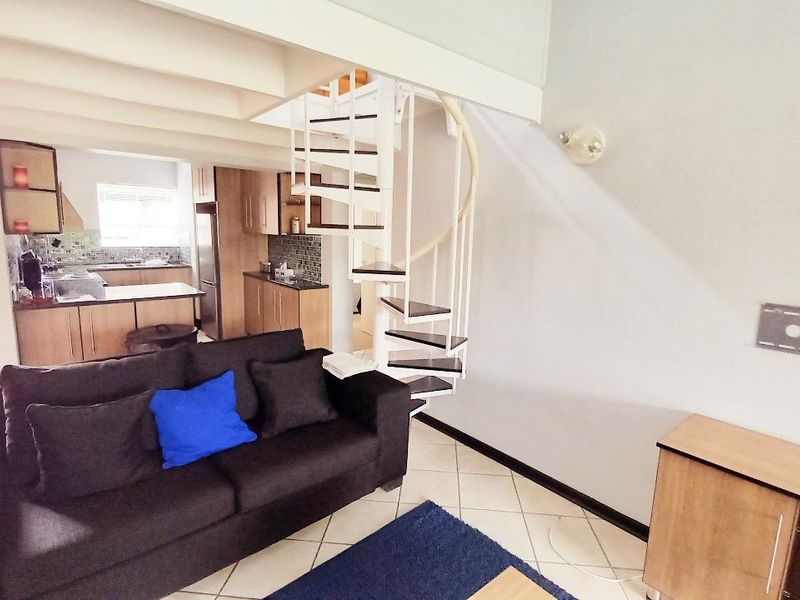 Open-plan living area featuring a spiral staircase, tiled flooring, and a functional kitchen with built-in cabinetry and countertops.