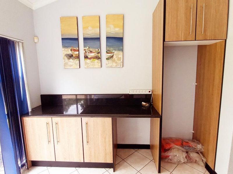 A functional scullery area featuring light wood-finish cabinetry, a dark granite countertop, and a dedicated alcove for a refrigerator.