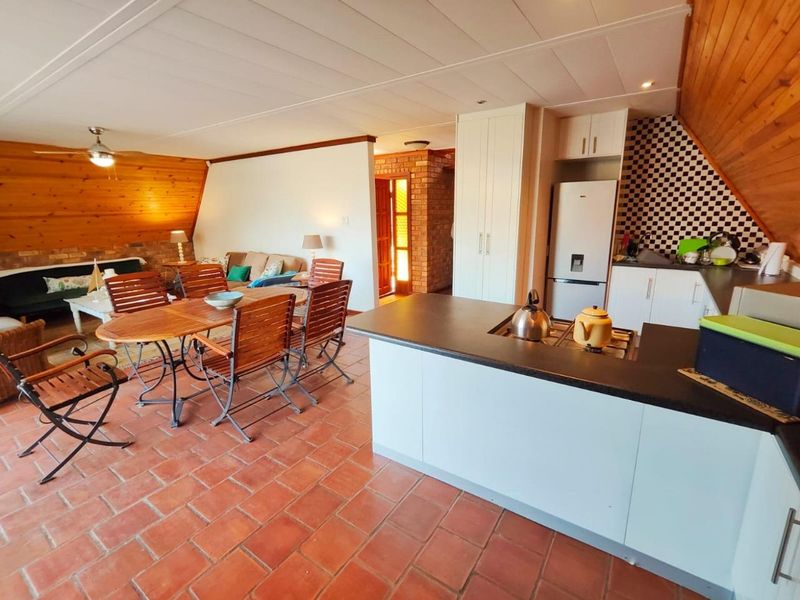 Open-plan living and kitchen area featuring terracotta flooring, timber wall paneling, exposed brick accents, and a functional kitchen with built-in cabinetry and gas hob.
