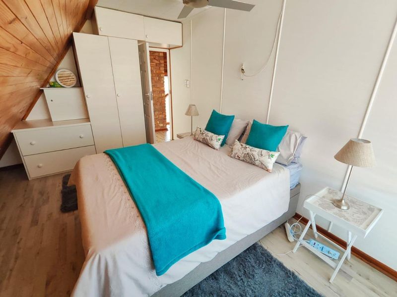 A bedroom featuring a sloped timber ceiling, built-in wardrobe, and laminate flooring, offering a cozy attic-style living space.
