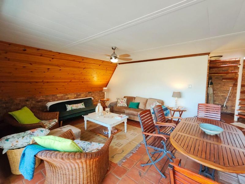 Spacious living area featuring a combination of exposed brick and timber paneling, complemented by traditional terracotta floor tiles and a ceiling fan.