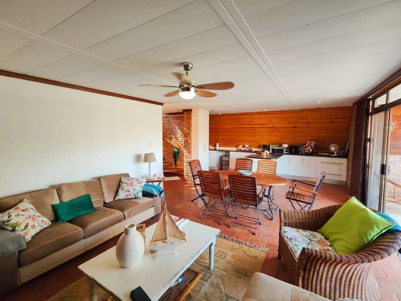 Spacious open-plan living and dining area featuring terracotta flooring, timber wall accents, and a functional kitchen with built-in cabinetry.