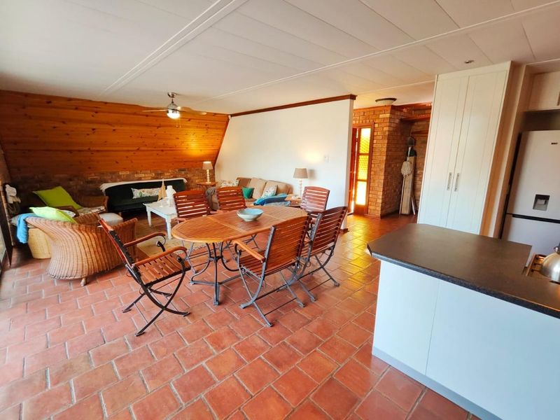 Open-plan living and dining area featuring terracotta floor tiles, timber wall paneling, exposed brick accents, and a functional kitchen with built-in cabinetry.