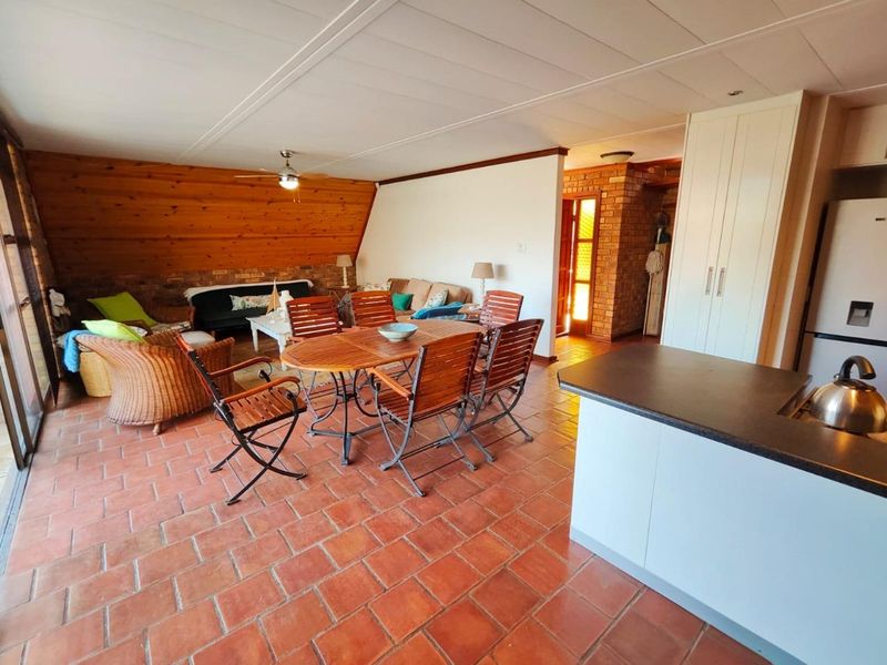 Spacious open-plan living and dining area featuring terracotta tile flooring, wood-paneled walls, and an exposed brick accent wall with integrated kitchen cabinetry.