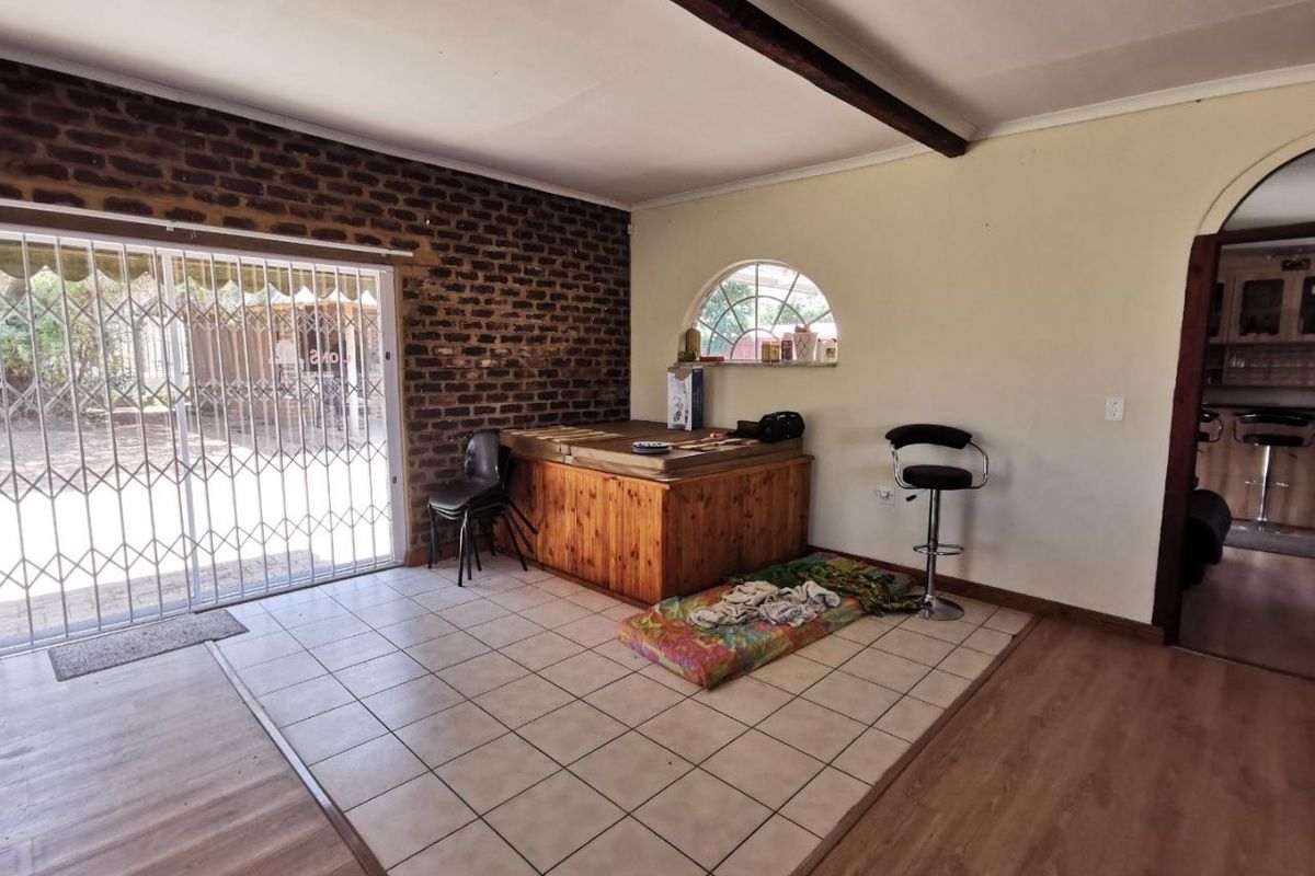 Living area featuring exposed brickwork, a mix of tiled and laminate flooring, and a sliding door with security gate leading to the exterior.