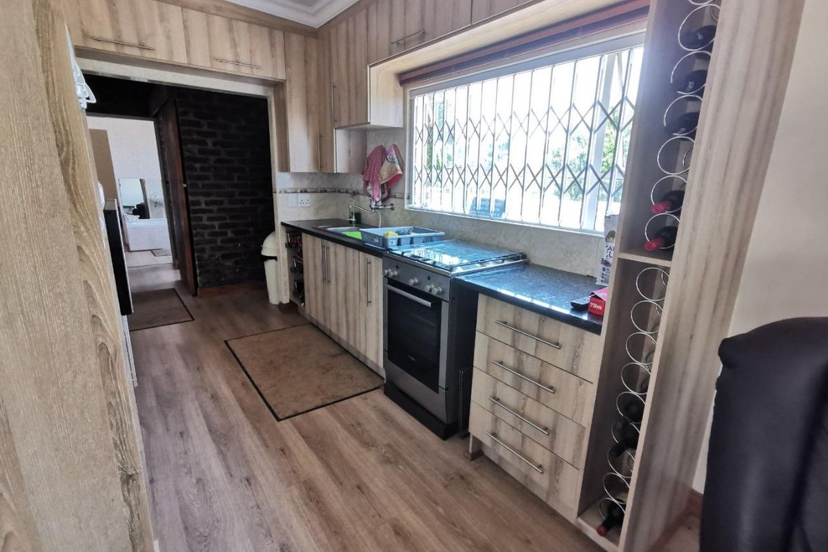 A functional kitchen featuring wood-look laminate cabinetry, granite countertops, a built-in wine rack, and a stainless steel stove with a window security gate.