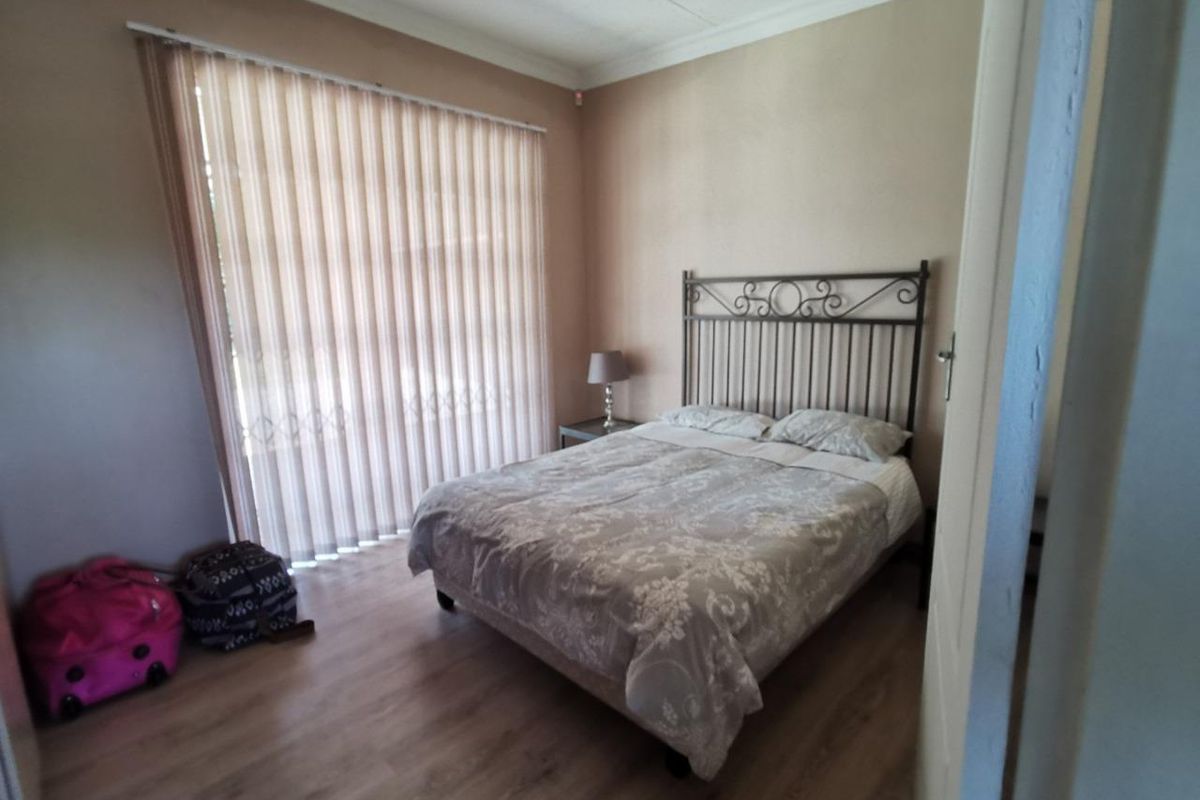 A bedroom featuring laminate flooring, coved ceilings, and vertical blinds covering a large window.