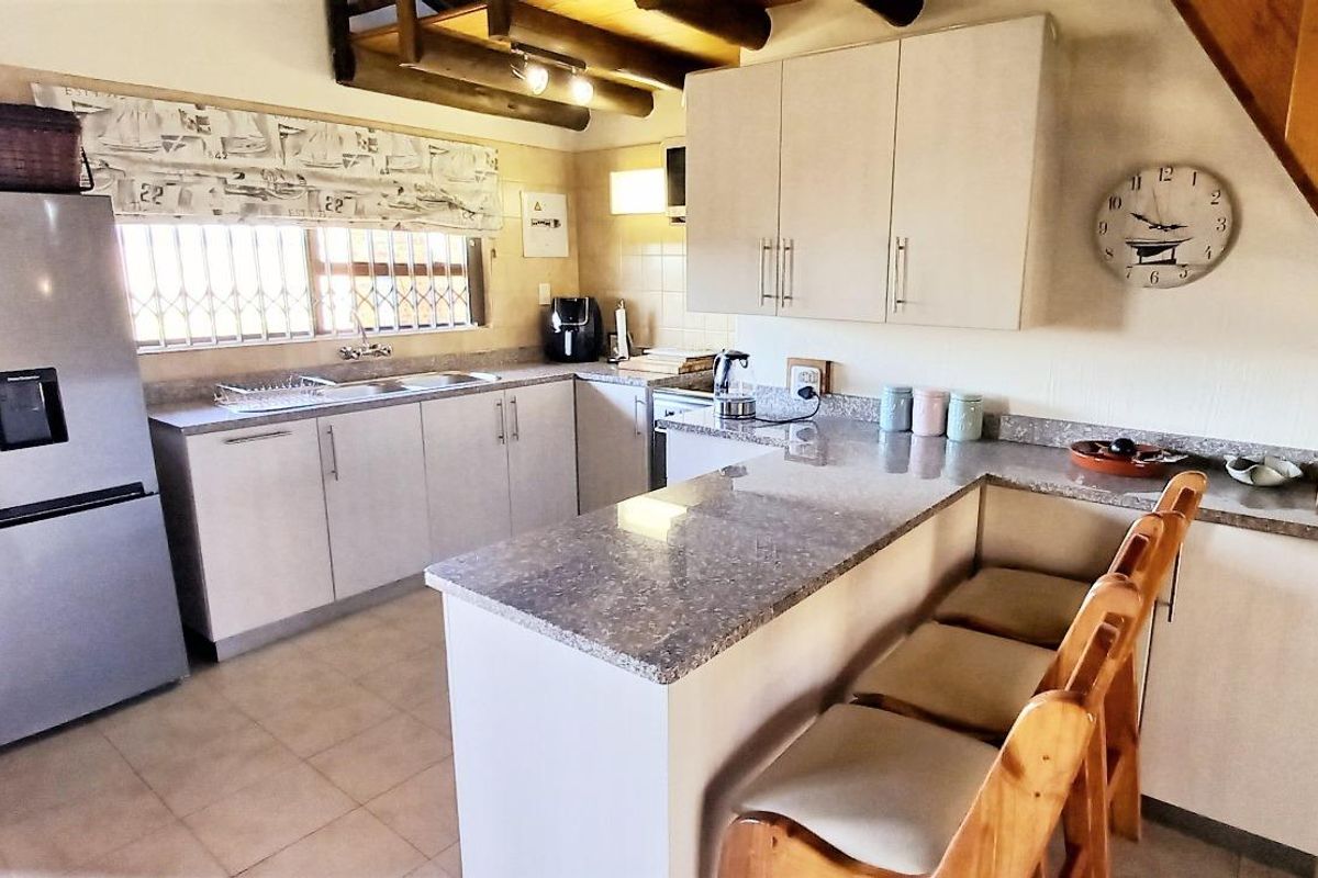 A functional kitchen featuring granite countertops, ample built-in cabinetry, a breakfast bar, and exposed timber ceiling beams.