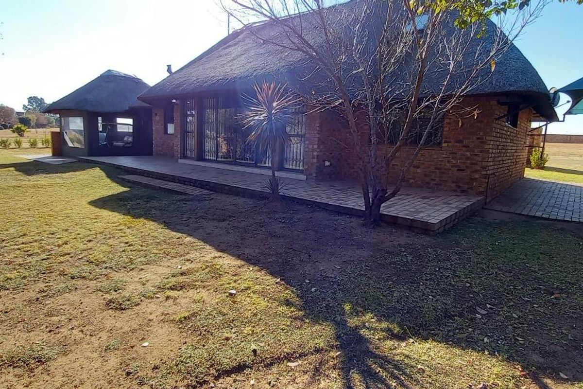 Rear view of a brick house with a thatched roof, featuring a paved patio area and a spacious garden.