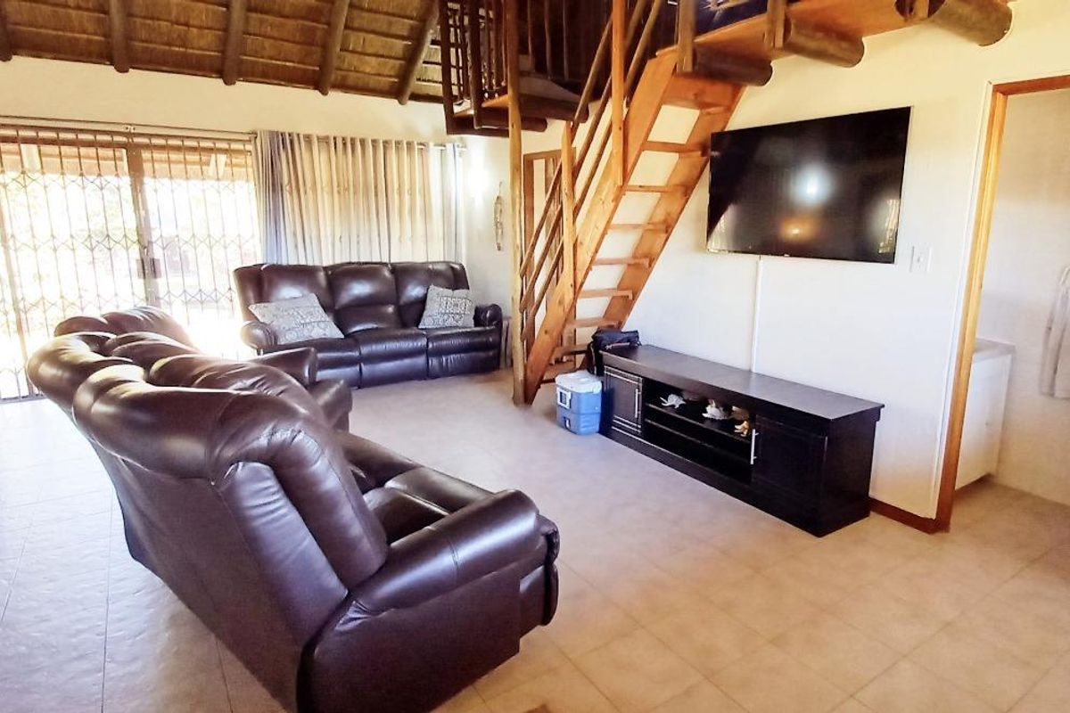 Spacious living area featuring a high thatch ceiling, timber staircase leading to a loft, and tiled flooring with access to an outdoor patio.