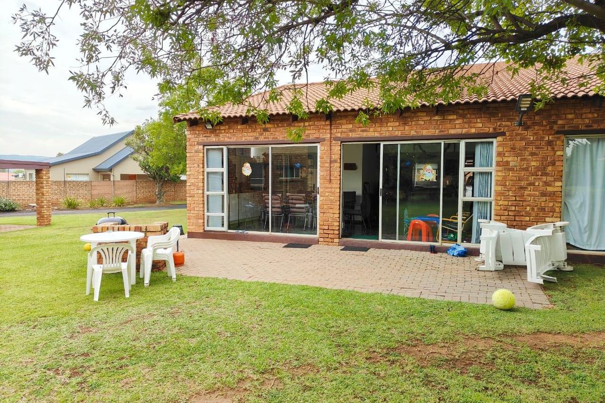 Rear view of the apartment featuring a brick facade, tiled roof, paved patio area, and sliding glass doors leading to the interior.