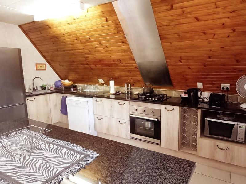 A functional kitchen featuring granite countertops, built-in oven, gas hob, and distinctive timber-clad sloped ceilings, offering a warm and practical cooking space.
