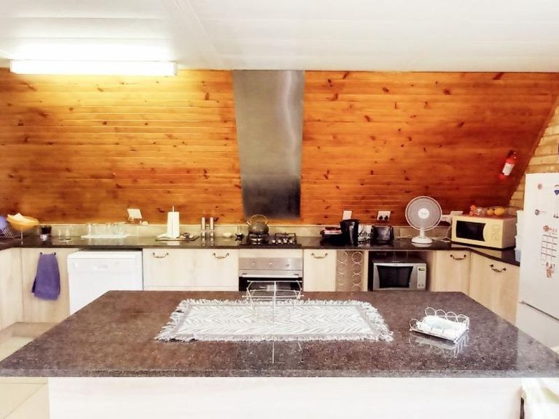 A functional kitchen featuring a central island with granite countertops, timber-clad walls, exposed brickwork, and integrated stainless steel appliances.