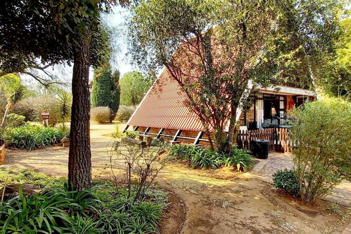 A view of the rear exterior of an A-frame house featuring a tiled roof, brick paved pathways, and established garden surroundings.