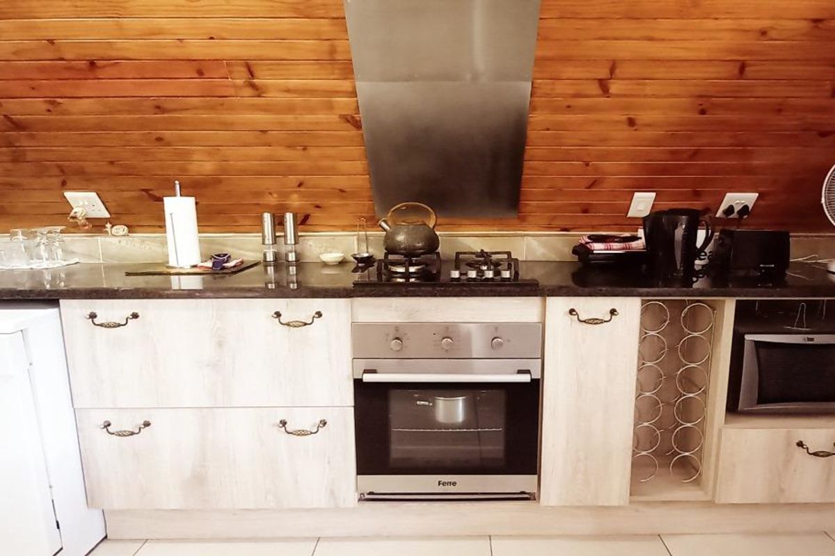 A functional kitchen featuring light wood cabinetry, granite countertops, a built-in oven with gas hob, and distinctive timber-clad walls.