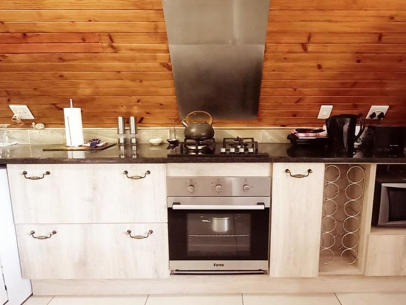 A functional kitchen featuring light wood cabinetry, granite countertops, a built-in oven with gas hob, and distinctive timber-clad walls.