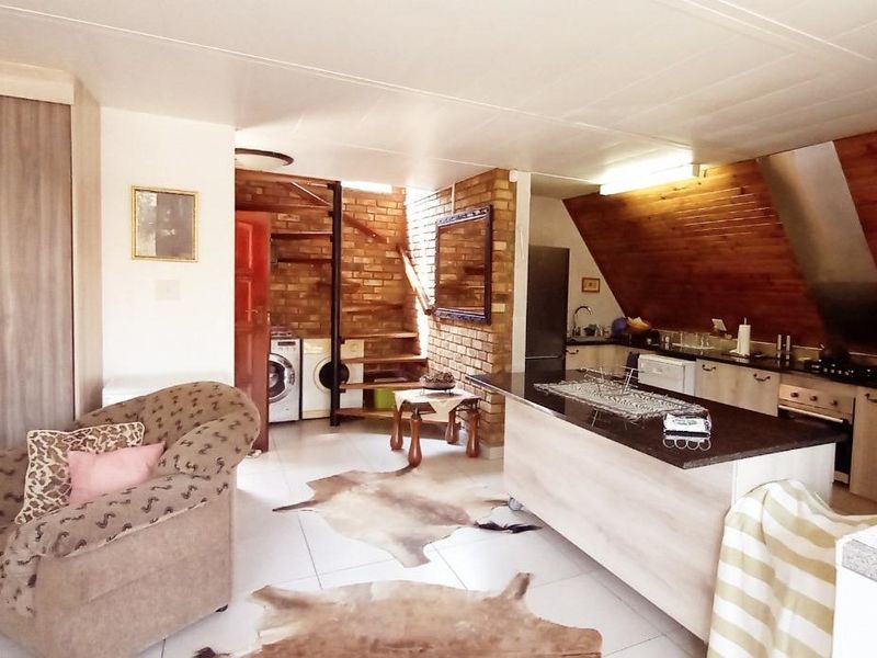 Open-plan living area featuring a kitchen with island, built-in appliances, exposed brickwork, and timber-clad ceiling, creating a rustic and functional space.