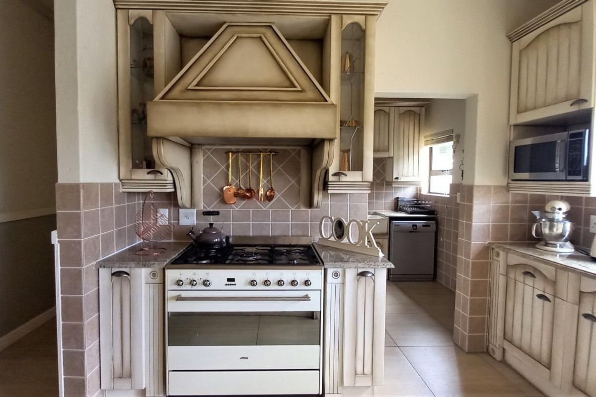 A traditional kitchen featuring a gas stove with a decorative extractor hood, granite countertops, tiled backsplash, and built-in cabinetry with an adjacent scullery area.