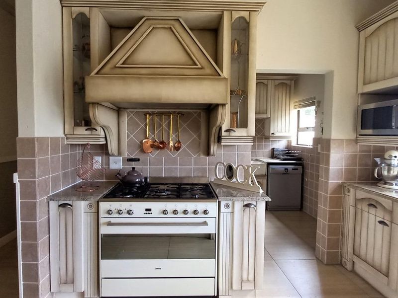 A traditional kitchen featuring a gas stove with a decorative extractor hood, granite countertops, tiled backsplash, and built-in cabinetry with an adjacent scullery area.