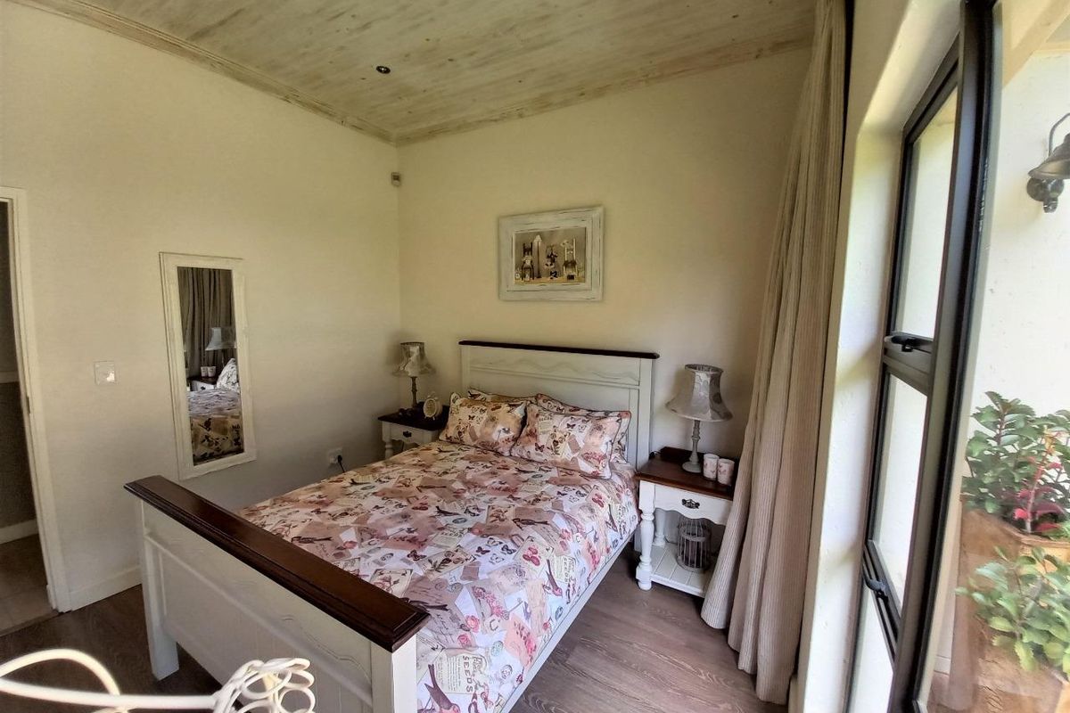 A cozy bedroom featuring timber-look flooring, a unique timber-clad ceiling with recessed lighting, and a large window providing natural light.