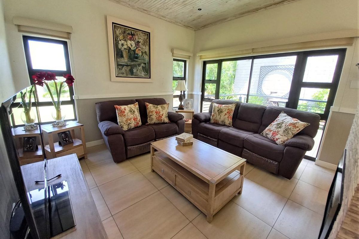 A bright living room featuring tiled floors, a timber-panelled ceiling, and large windows that provide ample natural light and access to the outdoor area.