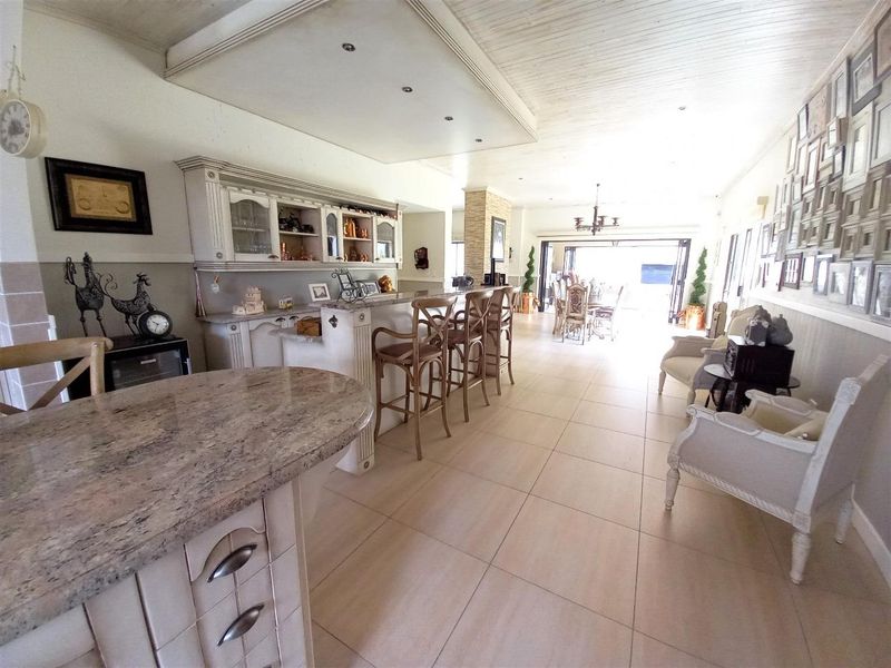 Spacious open-plan living area featuring a built-in bar with granite countertops, tiled flooring, and recessed lighting, leading towards an outdoor patio space.