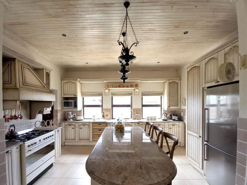 A spacious kitchen featuring custom cabinetry, a large stone-topped island, gas stove with extractor, and a distinctive timber-paneled ceiling.